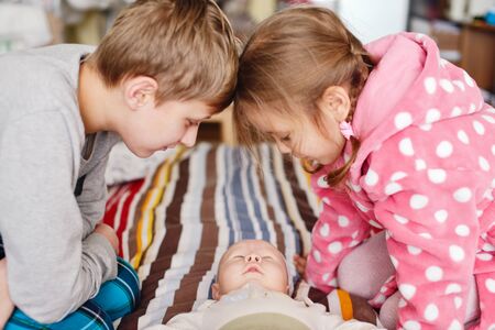 big brother and sister looking at baby brother at homeの写真素材