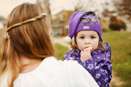 toddler girl on mothers hands eating biscuit in fallの写真素材