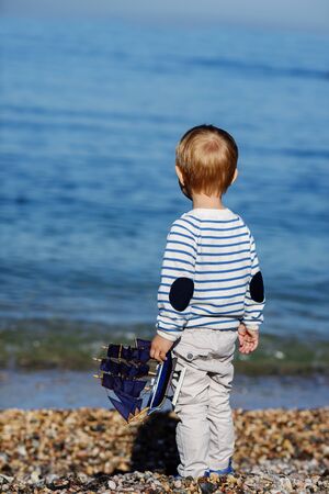 little boy standing near the sea and holding shipの写真素材