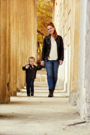 mother and toddler daughter walking on the street in fallの写真素材