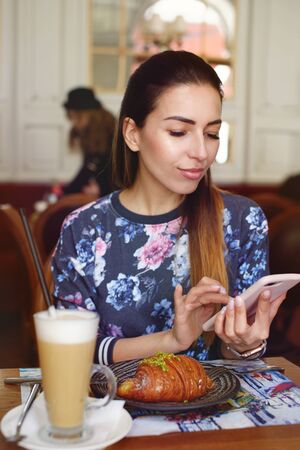 beautiful woman drinking coffee with croissant and using smart phone.の写真素材