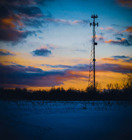 A vertical shot of a telecommunication tower in a snowy field under a colorful sunset