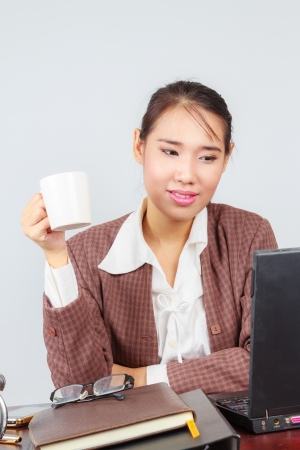 Portrait of a happy young business woman drinking coffee while working on laptop in officeの写真素材