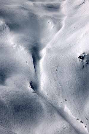 Aerial view of snow covered alpine mountain slopes in sunny winter day.