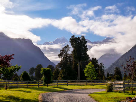 garden, meadow and trees, with mountain, cloud and blue sky in backgroundの写真素材