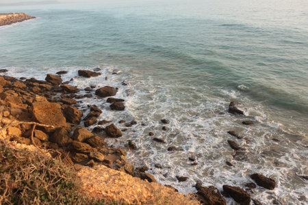 Ocean waves crashing on rocks below cliff at sunsetの写真素材