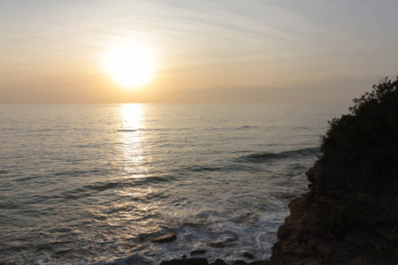 Golden sunset illuminating calm ocean from rocky cliffの写真素材
