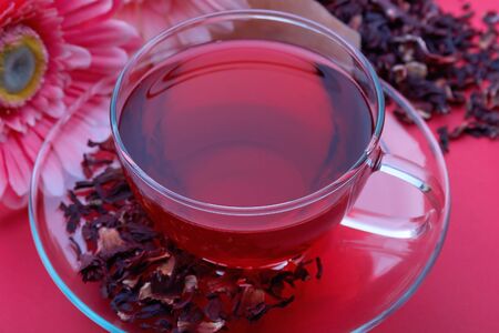 A cup of red karkade with scattered leaves of teaの写真素材
