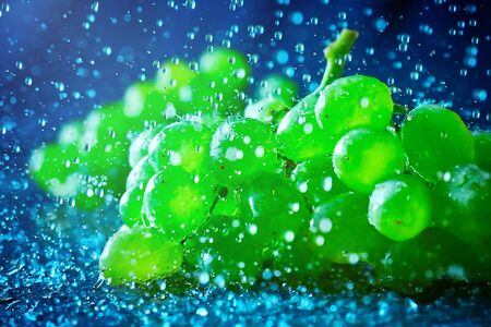 Ripe green grapes in splashes on blue backgroundの写真素材