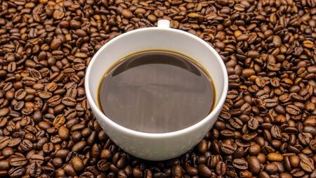 A cup of black coffee over roasted coffee beans