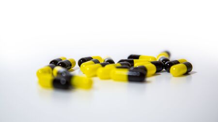 Close up of many black and yellow pills and tablets medicine isolated on white background. Prescription drugs. Medication, painkillers and drug abuse concept.の写真素材