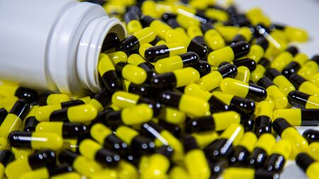 Close up on a bottle of prescription drugs falling out. Black and yellow pills and tablets medicine isolated on white background. A lot of medication, painkillers and drug abuse concept.の写真素材