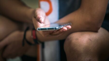Young man looking at smart phone after practicing sport. Athlete with a towel relaxing on room and...