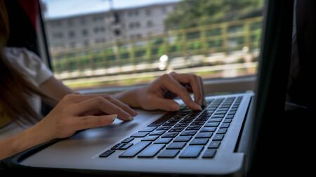 Businesswoman working with computer in the travel train. Asian young woman sit down near to window in higth speed rail checks her computer. Girl Works with Laptop. Programming writing. Studentの写真素材