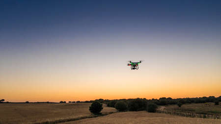 Aerial view of drone quadcopter flying with a digital camera over a field with sunset sky. Rural countryside landscape in Spain. Beautiful scenery under orange sunlight. Modern new technology.の写真素材