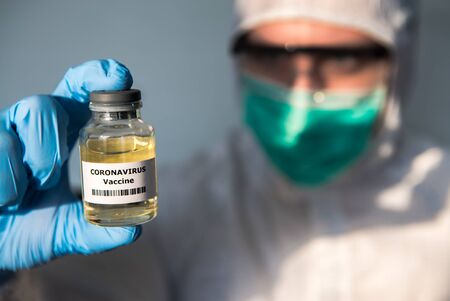 Doctor in protective suit and mask with a vaccine vial coronavirus. Preventive measures against Covid-19 infection. Epidemic virus outbreak concept. Medical and health care concept, Biological hazardの写真素材