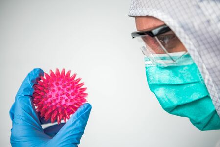 Hands of medical doctor with Corona virus model. Male scientific on protective suit holding a Coronavirus. Caucasian man with molecule of covid-19. Abstract model of a strain of the MERS-Cov virus.の写真素材