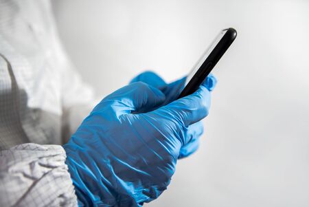 Scientist using smartphone in the scientific chemical laboratory. Doctor hands with blue gloves...