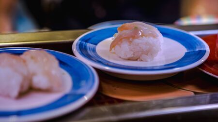 Sushi on conveyor belt in a Japan restaurant. Traditional Kaitenzushi Japanese food. Shushi Go Round is a famous form of fast food in Asia, also known as sushi train.の写真素材