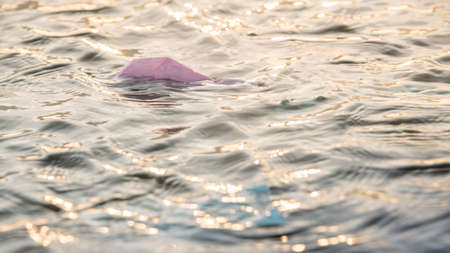 Coronavirus polluting the environment. The waves wash up old used medical mask waste. The personal protective equipment get into the water, they pose a threat to marine life.の写真素材