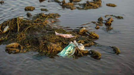 Coronavirus plastic waste polluting the environment. Disposable masks outbreak trash in the ocean. Discarded used disposable medical mask floats in sea watersの写真素材
