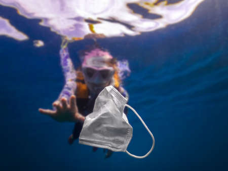 Volunteer woman scuba divers are exploring underwater and cleaning up the ocean. Catch a disposable masks outbreak trash on the blue water. Trash in the beach threatening the health of oceans.の写真素材