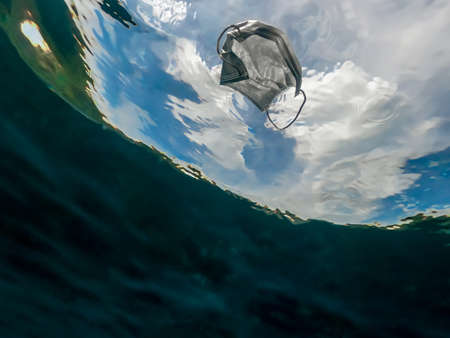 Protective mask discarded and thrown on the ocean. Abandoned facemask floating underwater of the sea. Used surgical masks for protection the coronavirus Covid-19.の写真素材