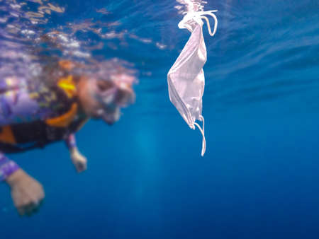 Volunteer woman scuba divers are exploring underwater and cleaning up the ocean. Catch a disposable masks outbreak trash on the blue water. Trash in the beach threatening the health of oceans.の写真素材