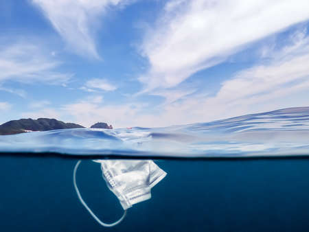 Protective mask discarded and thrown on the ocean. Abandoned facemask floating underwater of the...