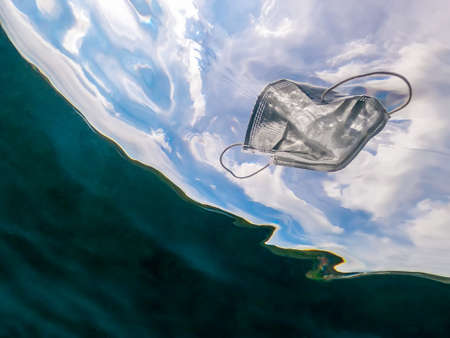 People throws out a medical face mask on the ocean water. Used surgical masks floating underwater of the sea. Useless coronavirus hygienic mask. Infectious wasteの写真素材