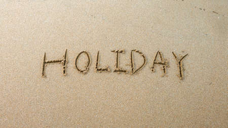 The Holiday word written on the sand of the shore beach with incoming wave washing, erasing or...
