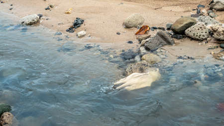 Coronavirus polluting the environment. The waves wash up old used medical gloves waste. Protective equipment get into the water, they pose a threat to marine life.の写真素材