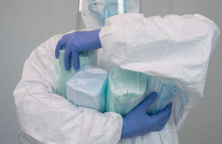 A nurse in a protective suit PPE has several packages of new masks and is picking up one. The health...