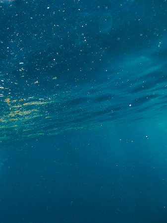 Sun light beams shining from above coming through the deep blue water causing a reflections curtain. Underwater ocean waves oscillate and flow. Scene light rays creates a beautiful veilの写真素材