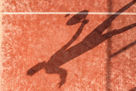 Shadow of a paddle tennis player with a racket in hand hitting the ball on an outdoor court.の写真素材