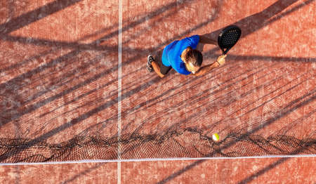 Top view of a professional paddle tennis player hitting the ball with the racket near the net of an...