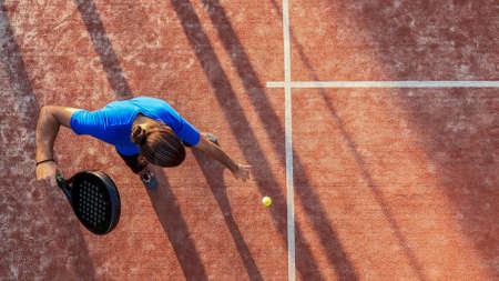 Top view of a paddle tennis player bouncing the ball for a serve on an outdoor court.の写真素材