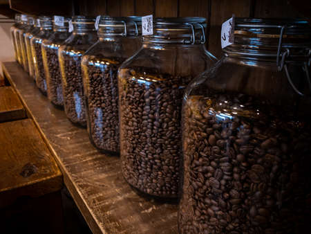 Black coffee beans glass jar packaging package on wood stand at caffe shop background. Freshly...
