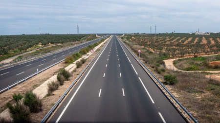 Aerial view of modern highway road on rural landscape outside the city. Two way asphalt road with country views in Andalusia with scattered and low clouds, a tree plantation of olives at Spainの写真素材