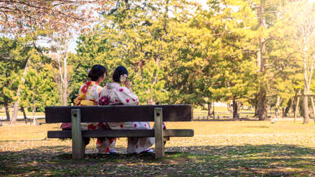 Maiko geisha sitting on the park bench of Nara. Two young pretty tourits women in kimono. Beautiful asian woman visit Japan in holidays. Japanese traditional asian style clothes dressのeditorial素材