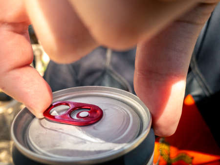Closeup of hand man holding and opening pull tab of soda or beer can. Hands open a metal aluminum beverage drink cola cans with natural sunlight at outsideの写真素材