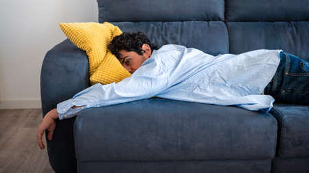 Despair man lying on the sofa and thinking about his problems. Portrait of tired alone serious man having problem in relationship. Unpleasant pain at home interior.の写真素材