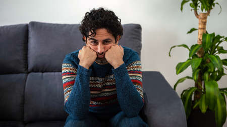Handsome male model feels tired after work. Mature man holding his forehead while having headache while sitting on couch home. Unpleasant pain.の写真素材