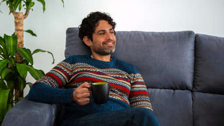 Handsome male model feeling happy and having a cafe. Caucasian man drinking morning expresso coffee while lying down on couch home. Modern lifestyle concept.の写真素材