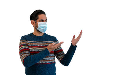 Caucasian man pointing with two hands to the side with medical mask during virus outbreak. Person looking to copy space aside for promotional text or advertisement on white studio backgroundの写真素材