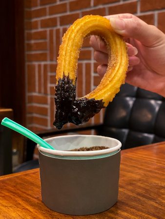 Woman eating a churro stick. Churros with sugar, chocolate and salted caramel sauce is a fried dough traditional Spanish dessert. Typical breakfast snack of Spain in the morningの写真素材