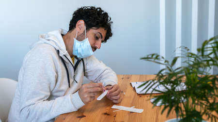 A man wearing mask placing the sample into the antigen diagnostic test device at home.