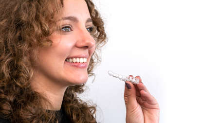 Smiling beautiful adult woman holds invisalign transparent braces in her hand. Caucasian person...