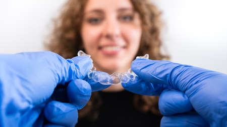 Orthodontist doctor in gloves holding silicone invisible transparent braces show to woman in dental...