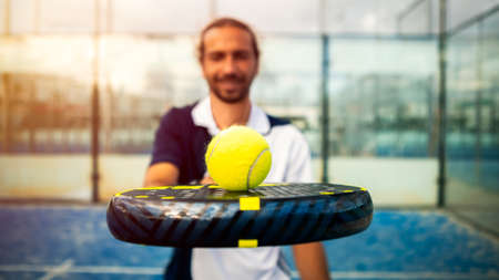 Monitor of padel holding black racket with yellow tennis ball over. Class to student on outdoor tennis court. Man paddel player playing a match in the openの写真素材
